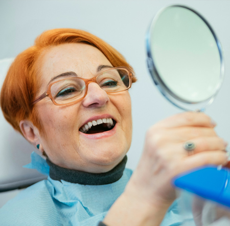 woman smiling in handheld mirror in dental chair. 